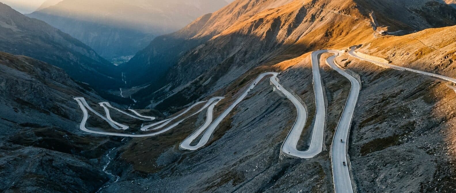 Luftaufnahme einer Alpenpassstrasse mit dutzenden Serpentinen im Abendlicht